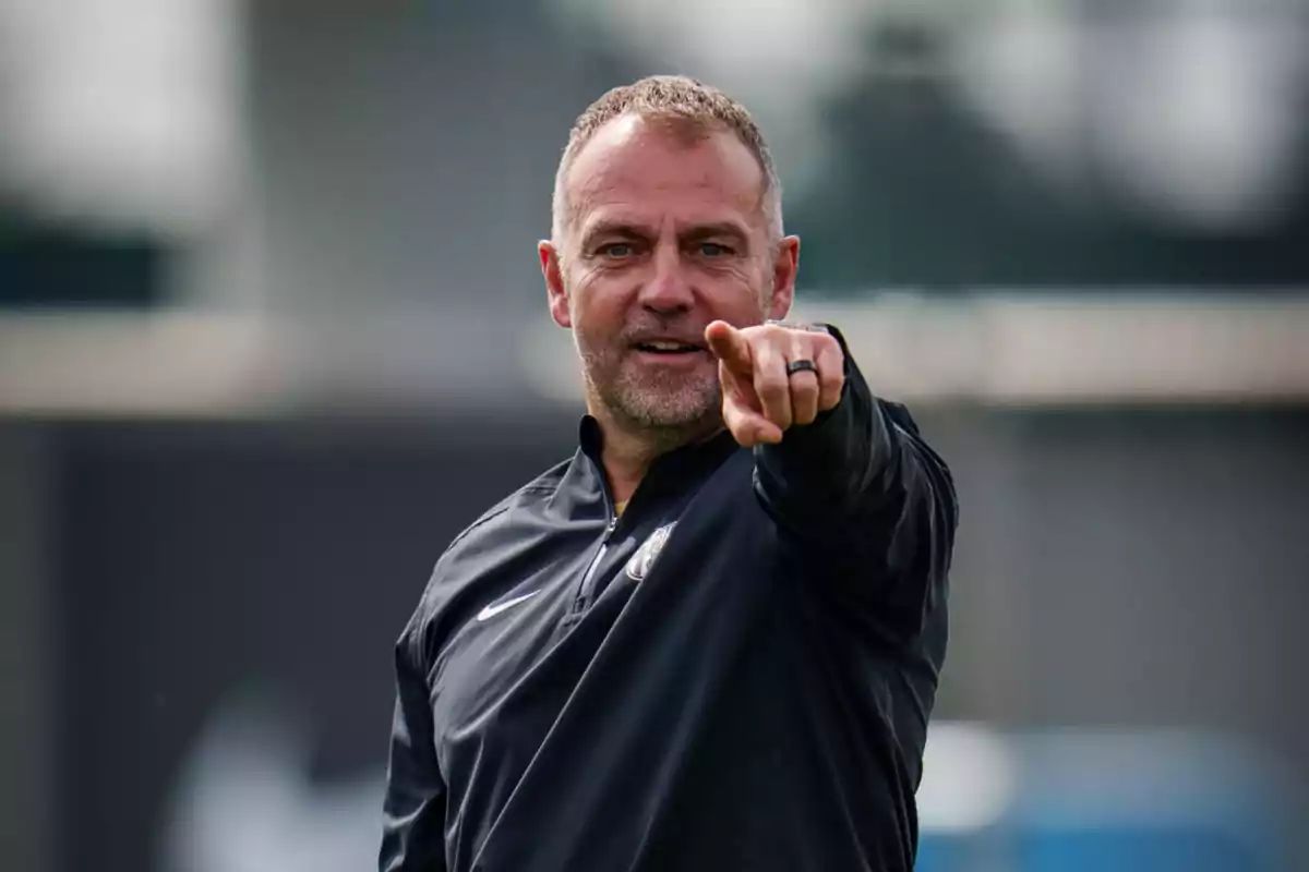 A man in a black sports jacket pointing forward with his index finger.